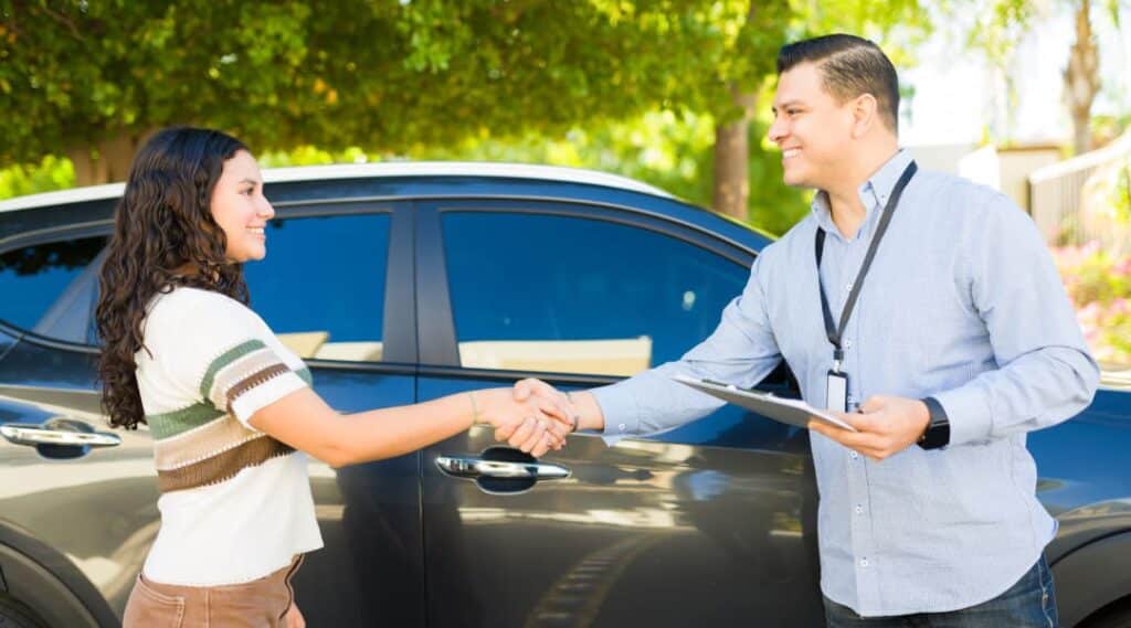 Praktische Fahrprüfung – Fahrprüfer begrüßt Kandidatin vor Beginn der Prüfung