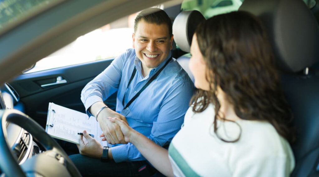 Praktische Fahrprüfung – Prüfer gratuliert Fahrschülerin nach bestandener Prüfung im Auto.