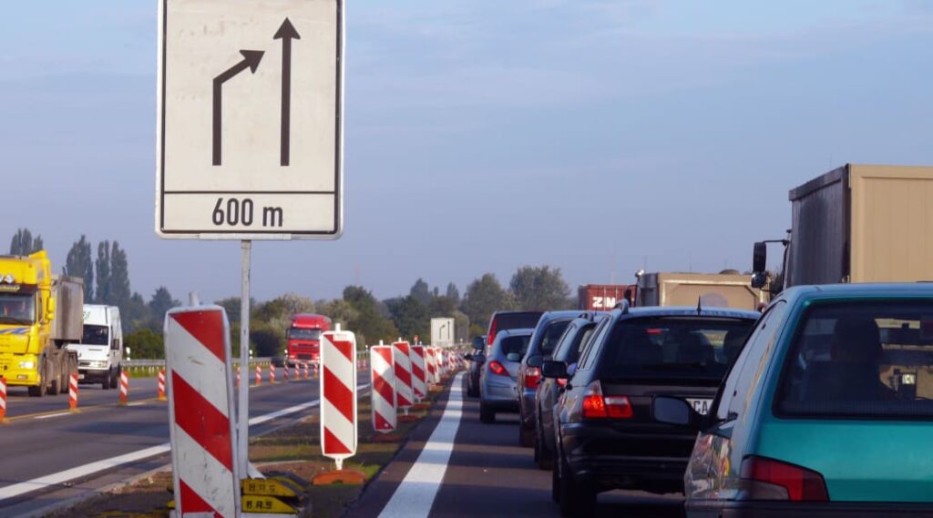 Autos im stockenden Verkehr vor einer Baustelle mit Spurabbau und Verkehrsschild zum Reissverschlussverkehr